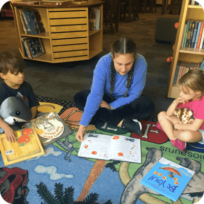 Older child reading to younger children in a library